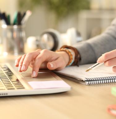 Person typing on laptop and in notebook