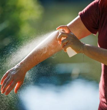 person spraying bug spray on their arm.