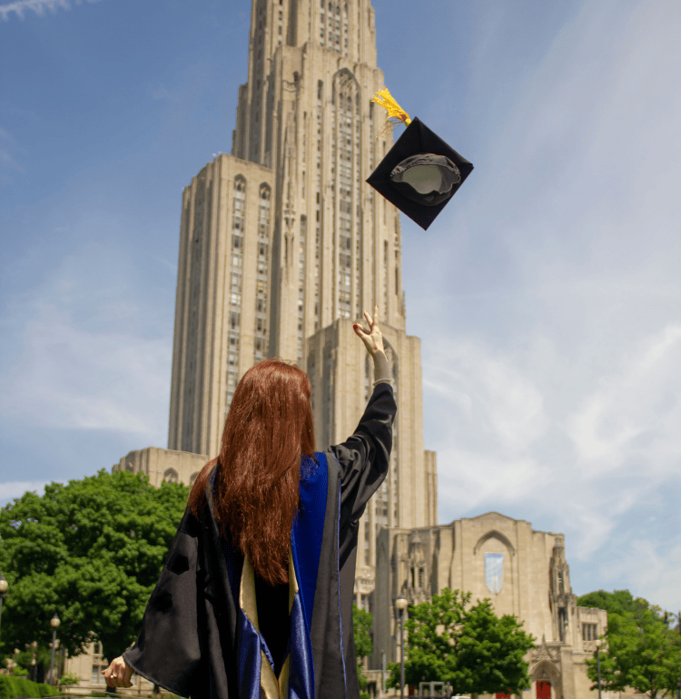 graduate throwing their cap in the air in front of the Cathedral of Learning